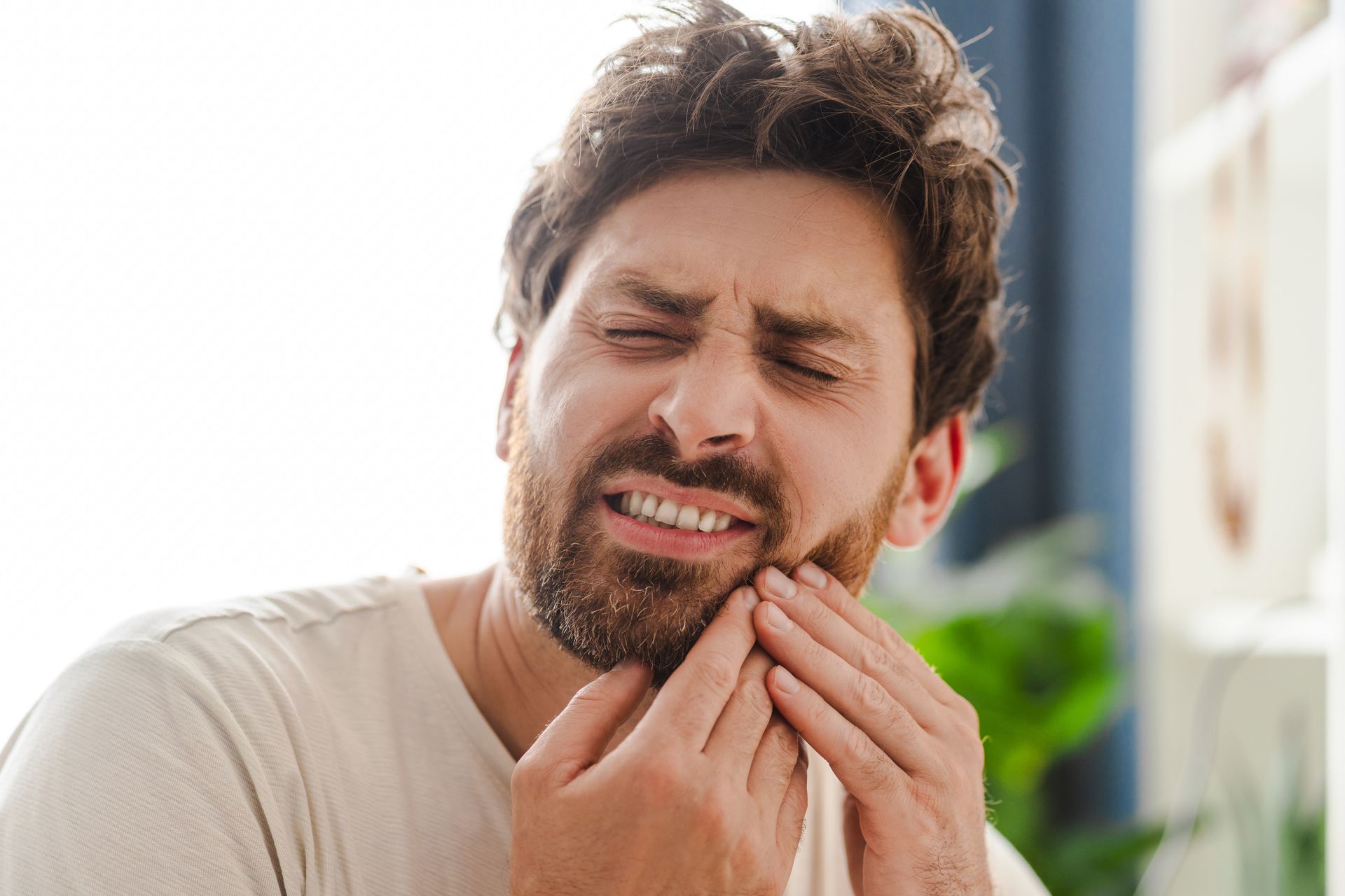 A man with a beard is holding his face in pain because he has a toothache.