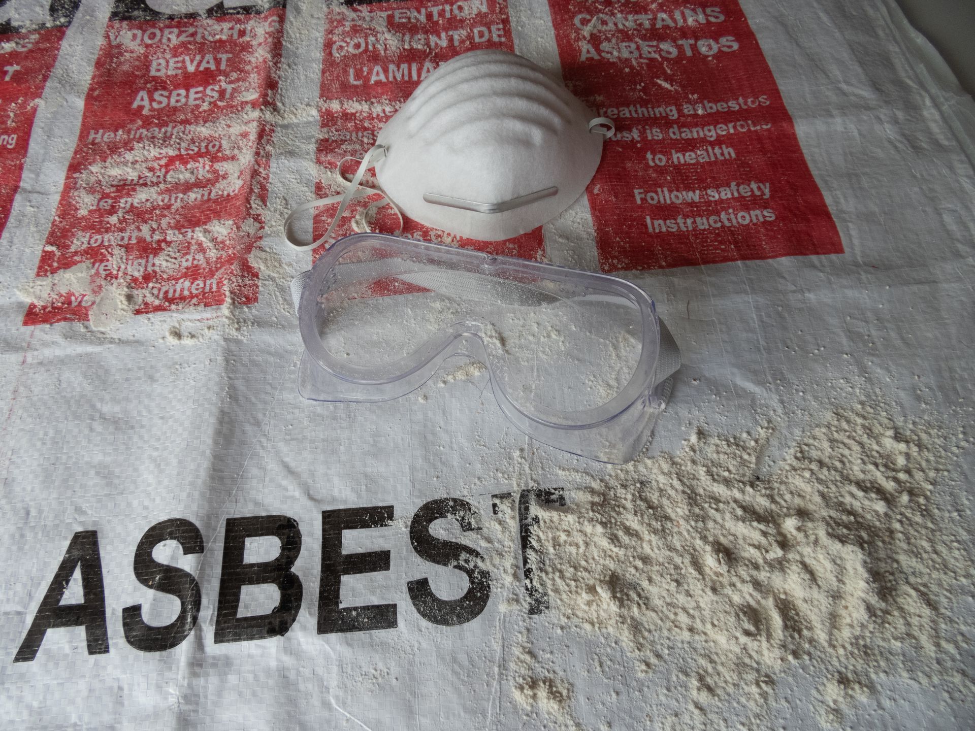 Asbestos fibers with a dust mask and safety goggles on a white bag labeled 