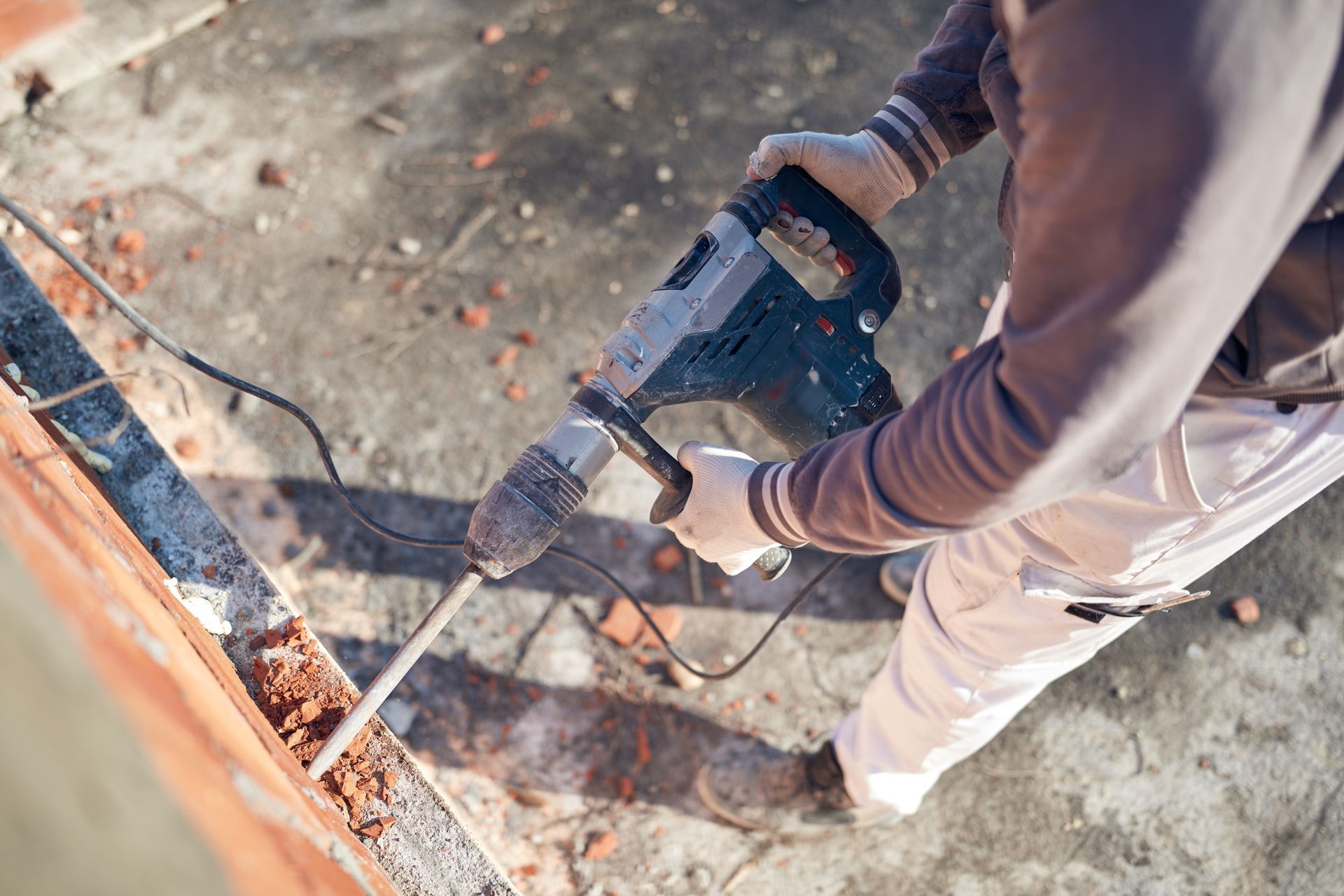 Person using a jackhammer on a concrete surface, removing debris.