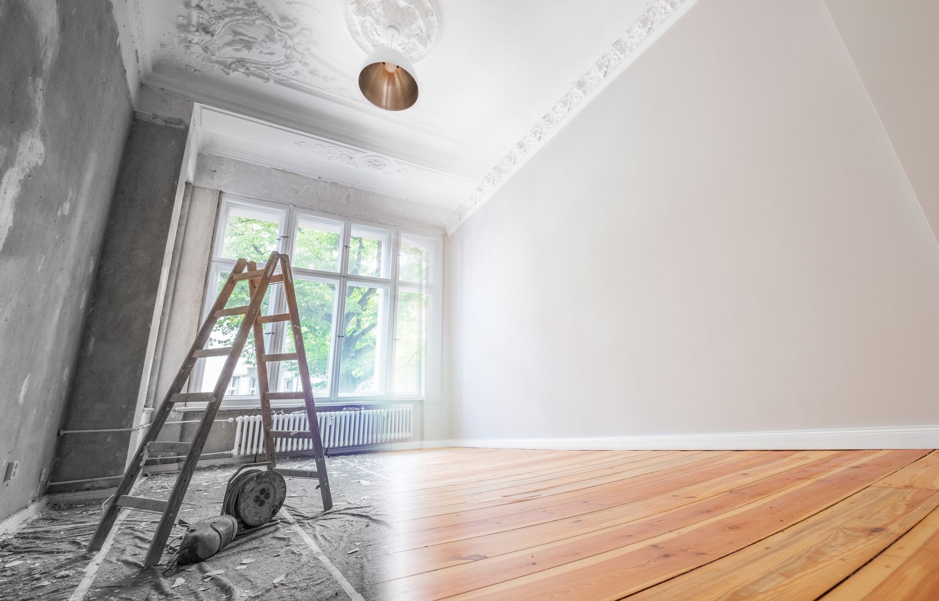 Room undergoing renovation; one side unfinished with ladder, other side painted white, hardwood floor.