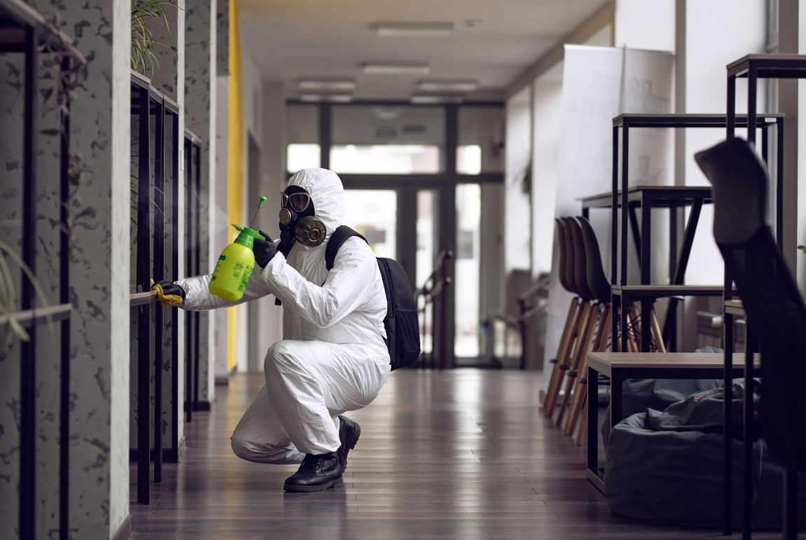 Person in hazmat suit disinfecting an office hallway with a sprayer.