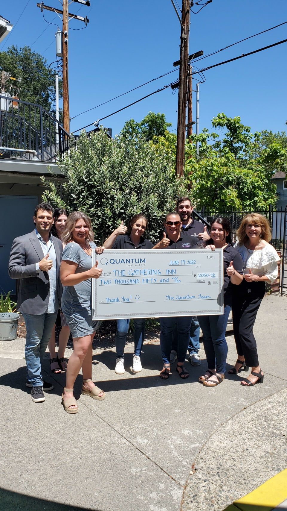 Group of people holding an oversized check outside. They smile and give thumbs up, celebrating a donation.