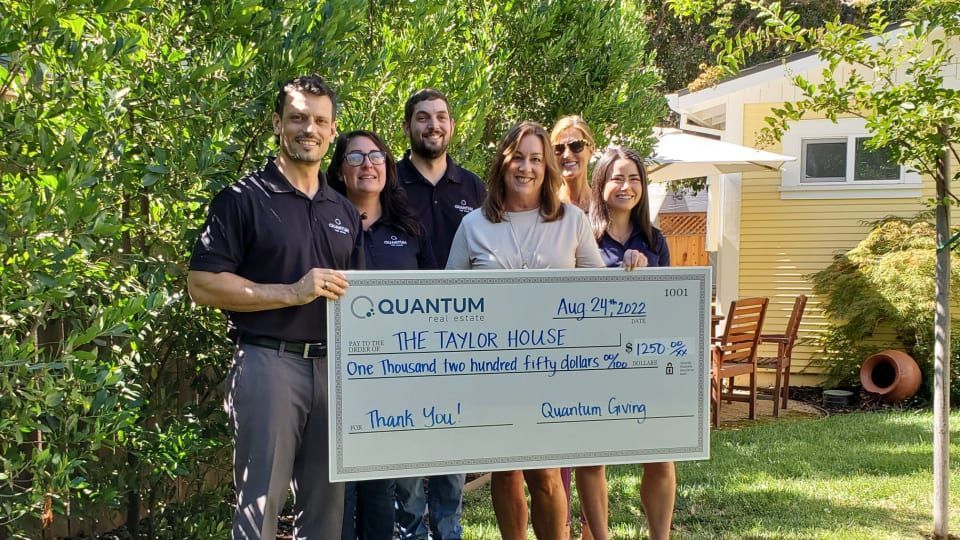 Group of people presenting a check to The Taylor House, outdoors.