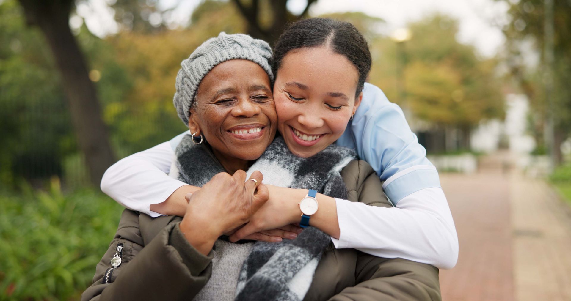 A young woman is hugging an older woman in a park.