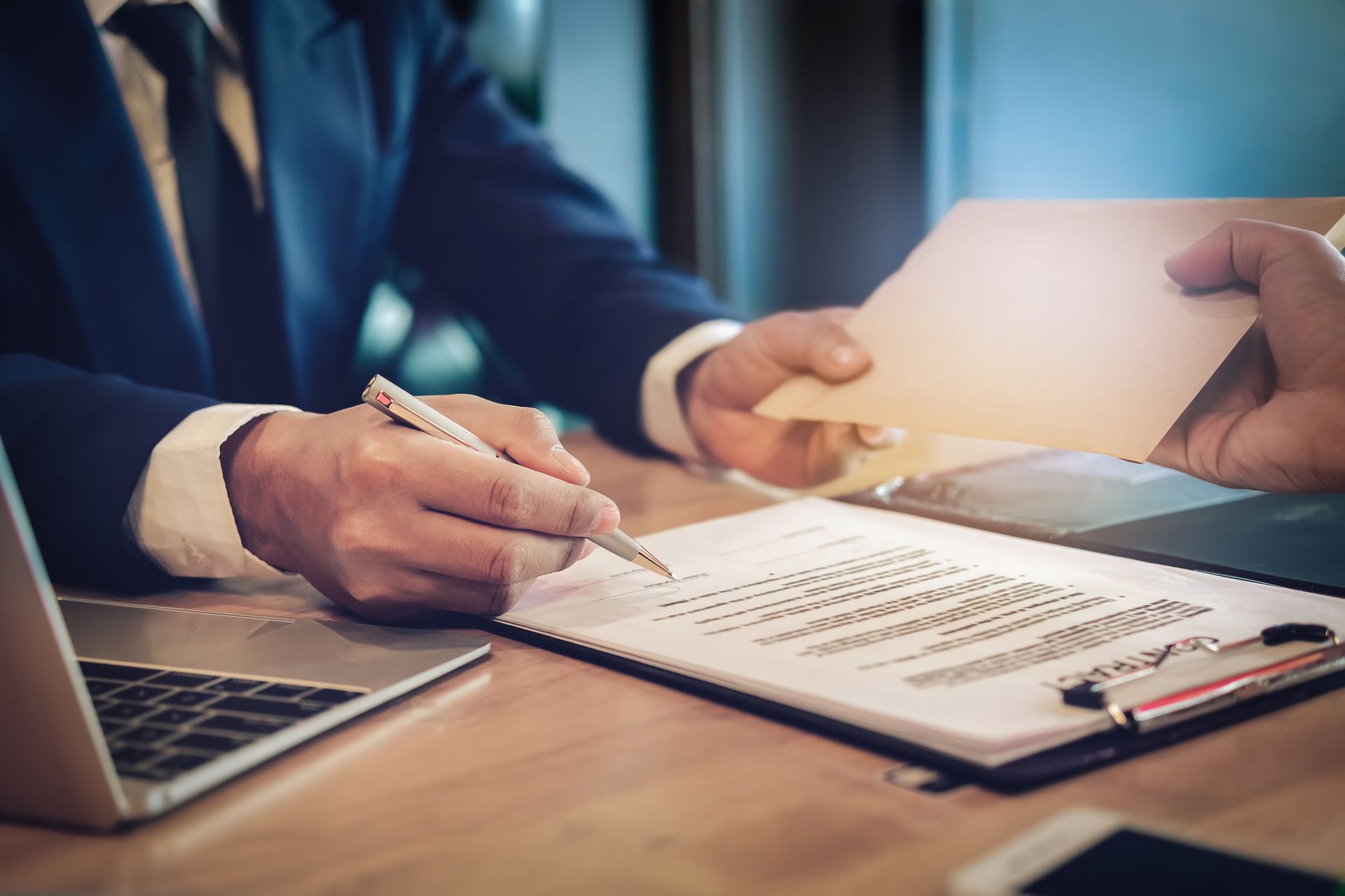 A man in a suit is sitting at a desk signing a document.