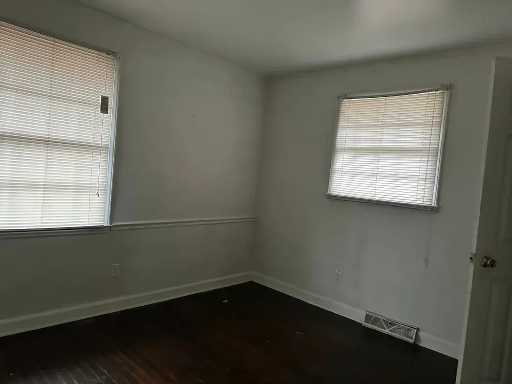 An empty room with two windows and a wooden floor.