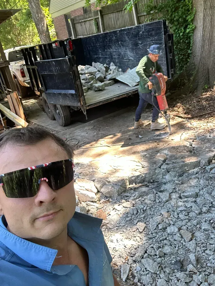 A man wearing sunglasses is standing next to a man using a hammer.