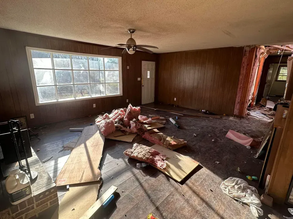 A living room with a ceiling fan and a lot of junk on the floor.