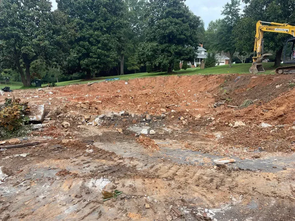 A large dirt field with a yellow excavator in the middle of it.