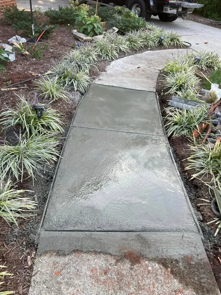 A concrete walkway surrounded by plants and a truck parked on the side of the road.