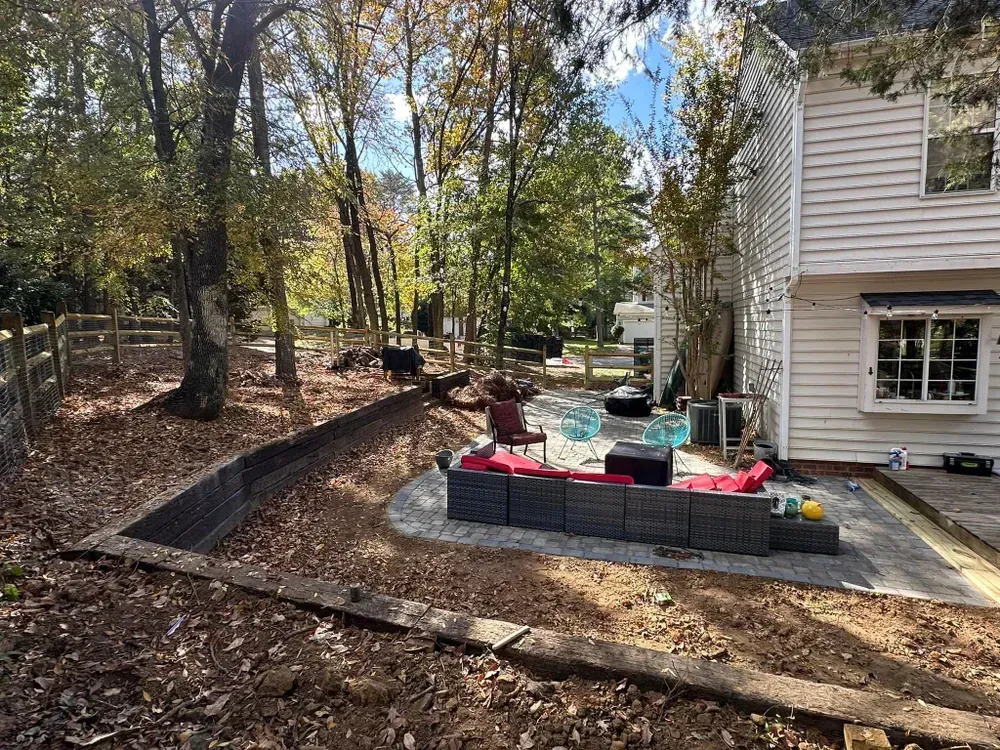 A patio with a couch and chairs in front of a house surrounded by trees.