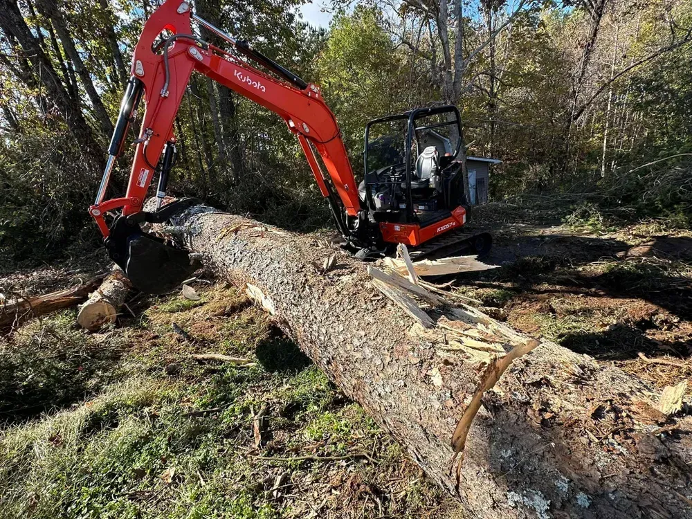A red excavator is moving a large log in the dirt.