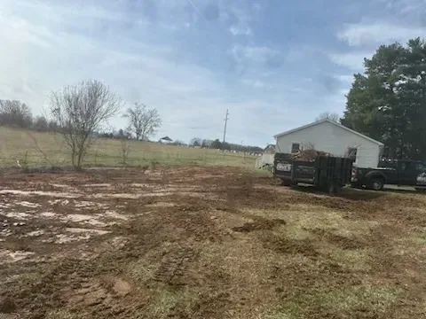 A truck is parked in a muddy field next to a house.