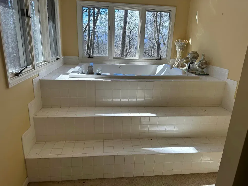 A bathtub with stairs leading up to it in a bathroom next to a window.