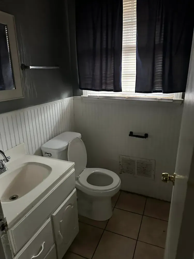 A bathroom with a toilet , sink , mirror and window.