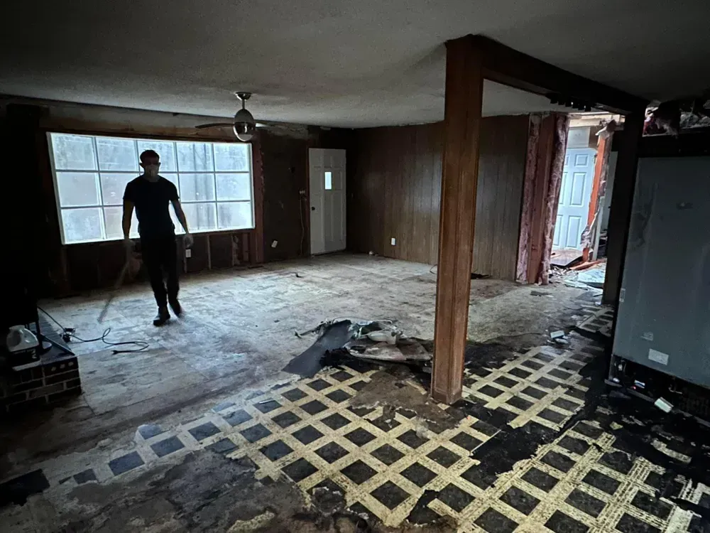 A man is standing in an empty room with a ceiling fan.