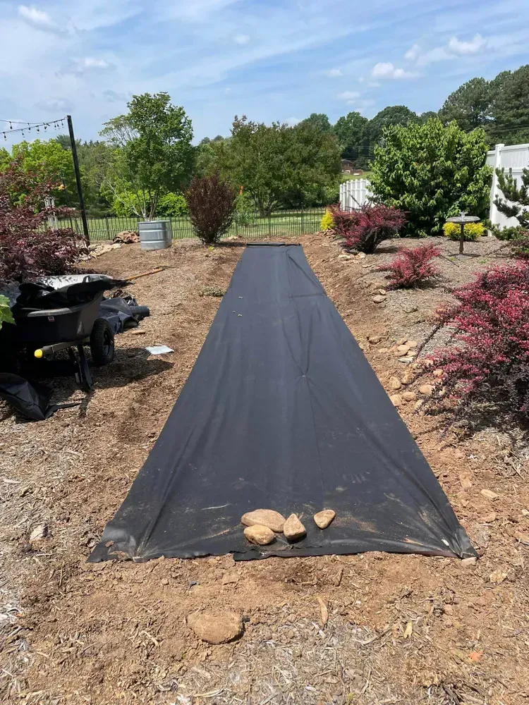 A black tarp is laying on the ground in a garden.