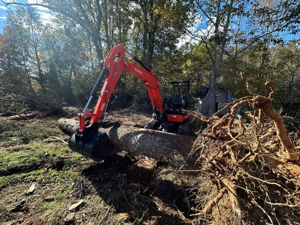 A red and black excavator is moving a large log in a field.
