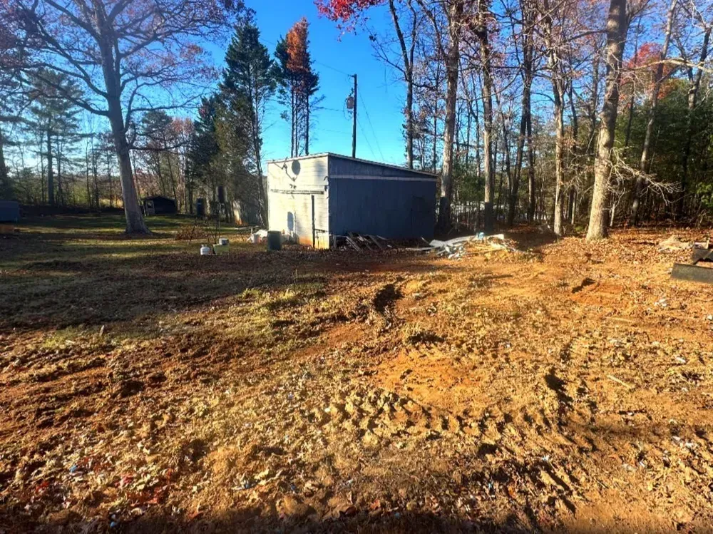 A shed is sitting in the middle of a dirt field surrounded by trees.