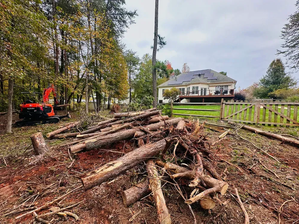 A pile of logs in a yard with a house in the background.