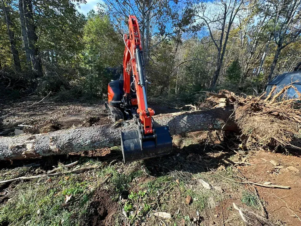 A small excavator is moving a large log in the dirt.