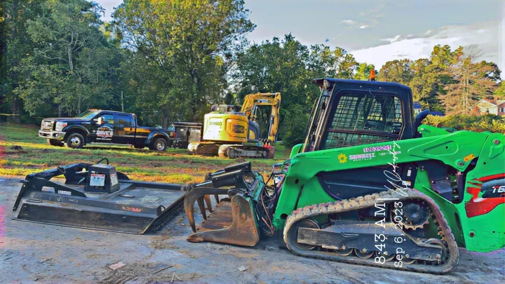A green bulldozer is parked in a dirt lot next to a truck.