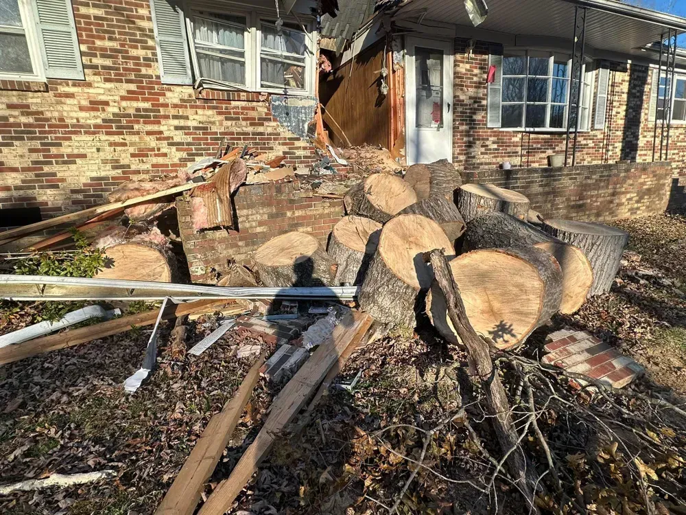 A pile of logs is sitting in front of a brick house.