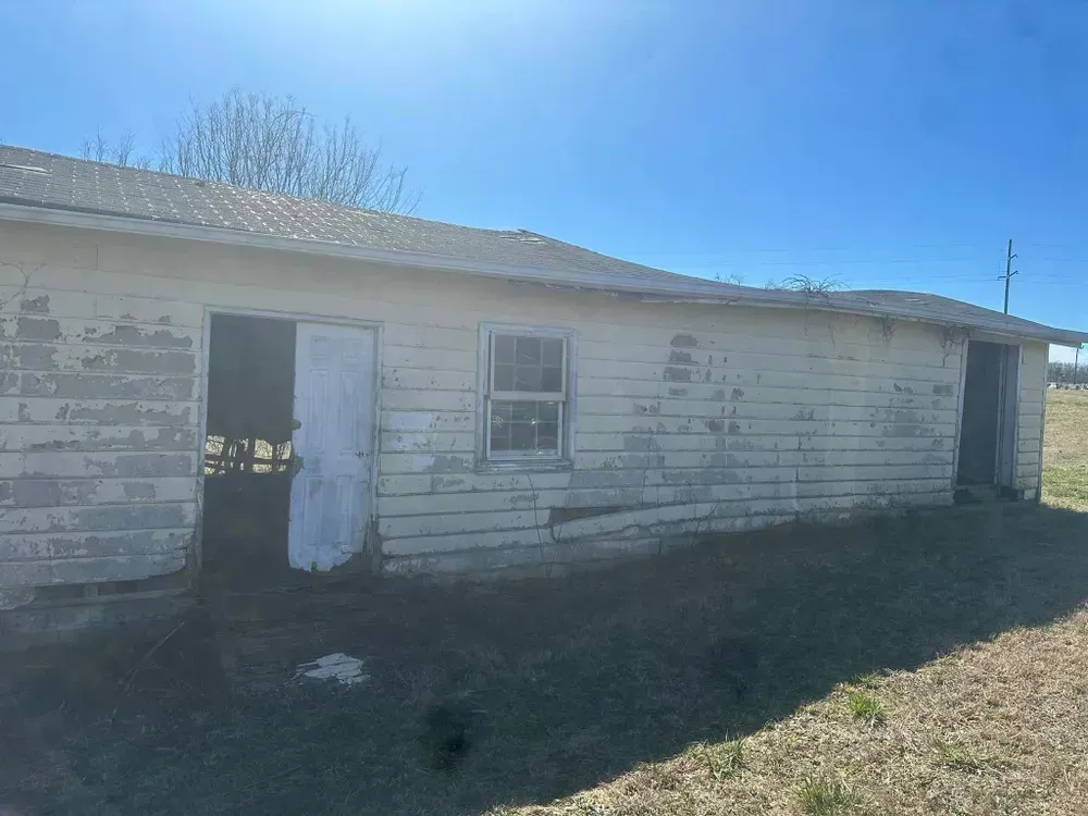 An old white house is sitting in the middle of a field.