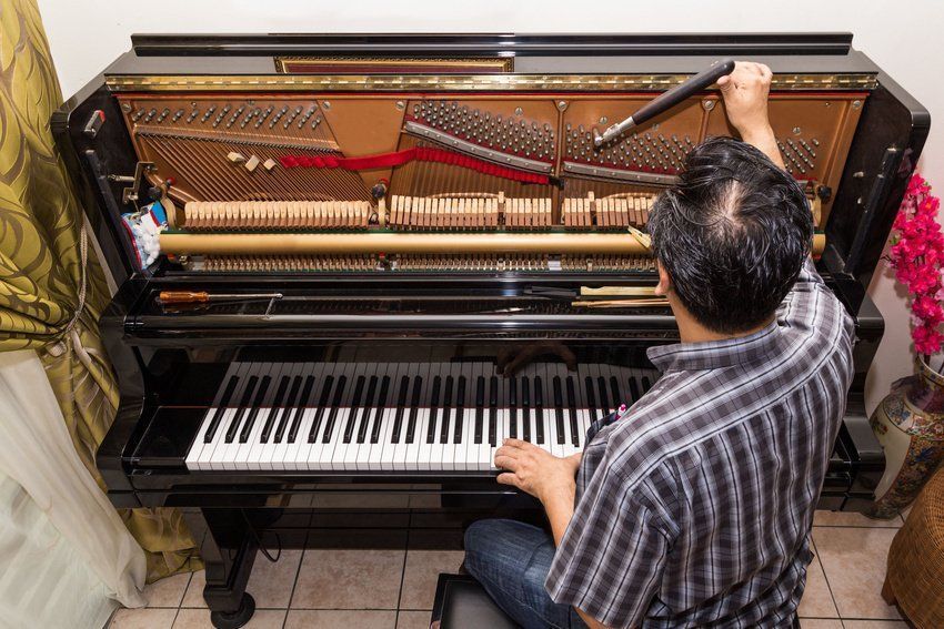 A man is repairing a piano in a living room.