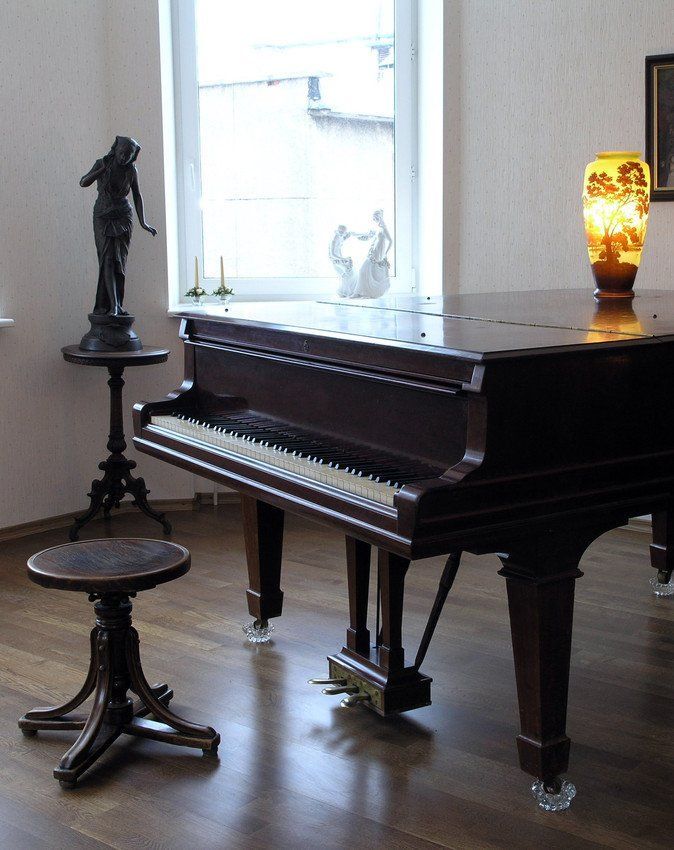 A piano in a room with a lamp and a statue.
