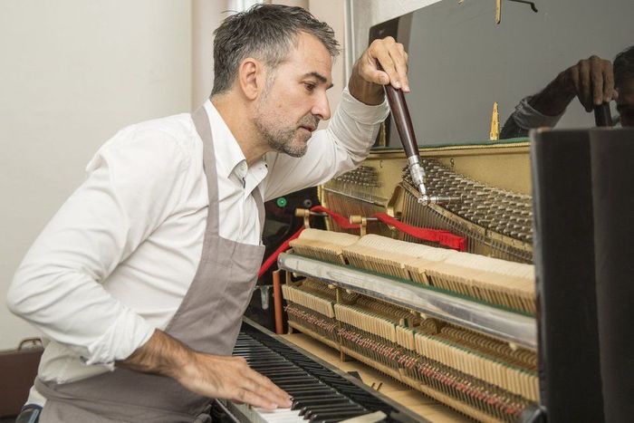 A man in an apron is working on a piano.