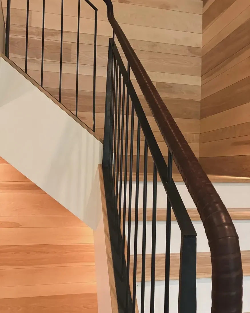 Wooden staircase with a dark metal railing and wood paneled wall.