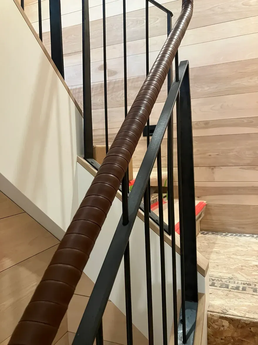 Staircase with wooden steps and a dark metal railing with a leather-wrapped handrail.