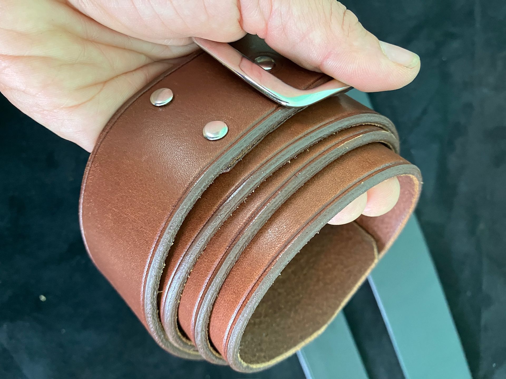 Hand holding a coiled brown leather belt with a silver buckle and studs.