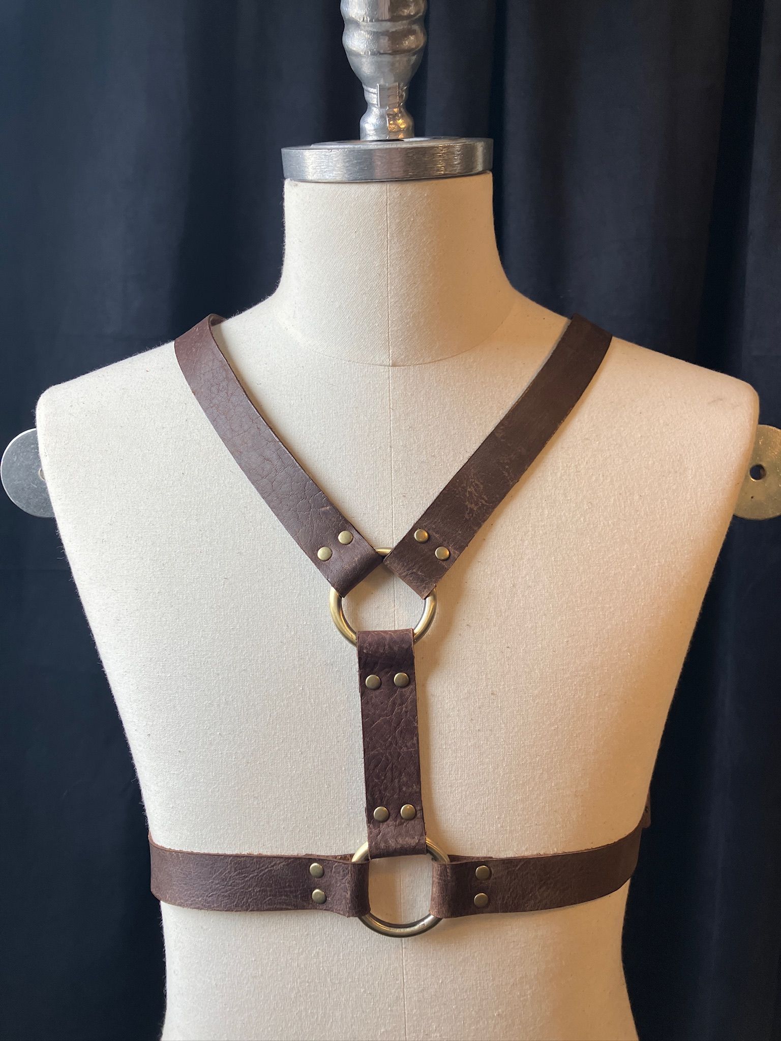 Brown leather body harness on a mannequin, with metal ring details.
