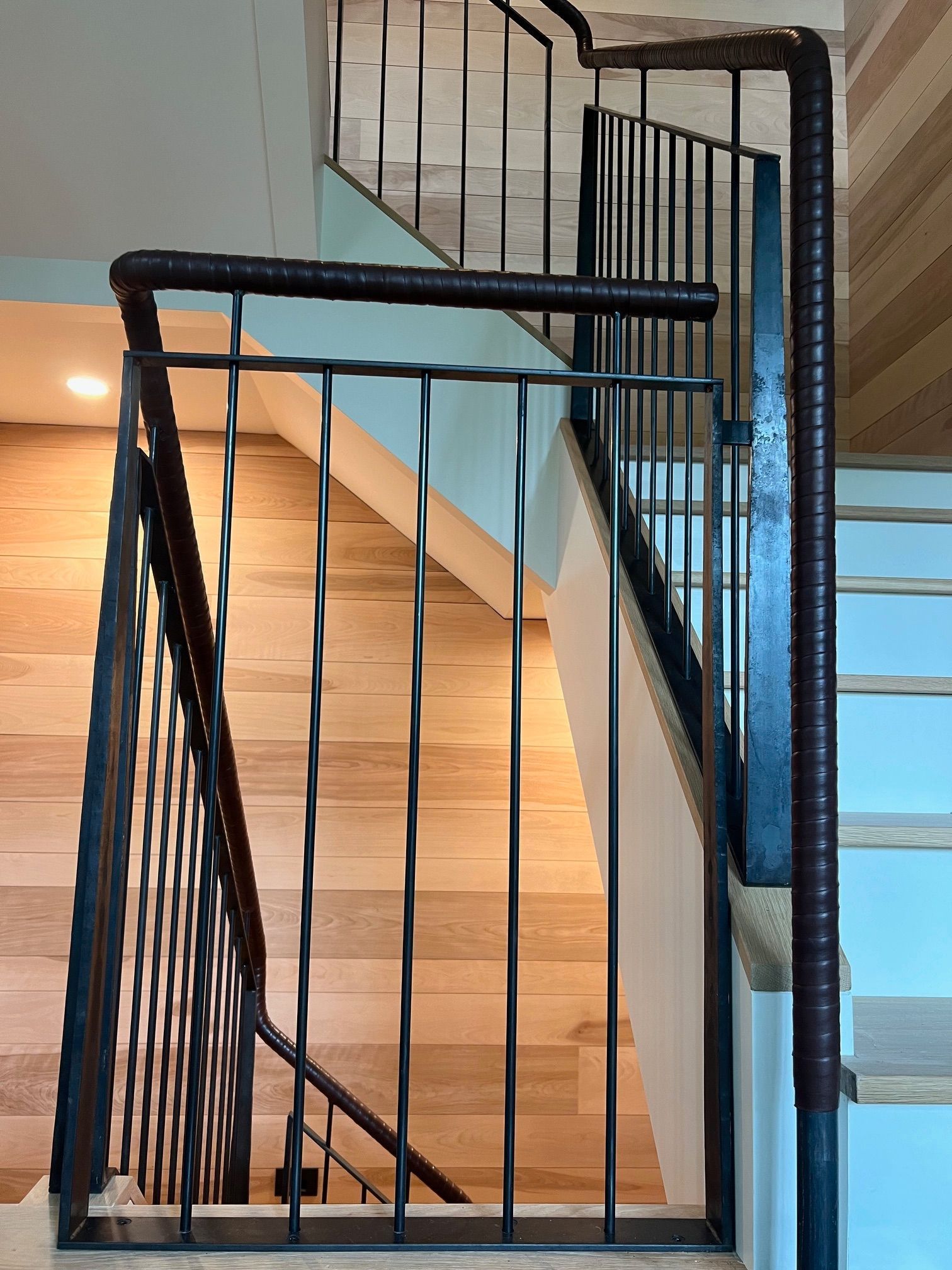 A staircase with a metal railing and wooden steps featuring leather trim