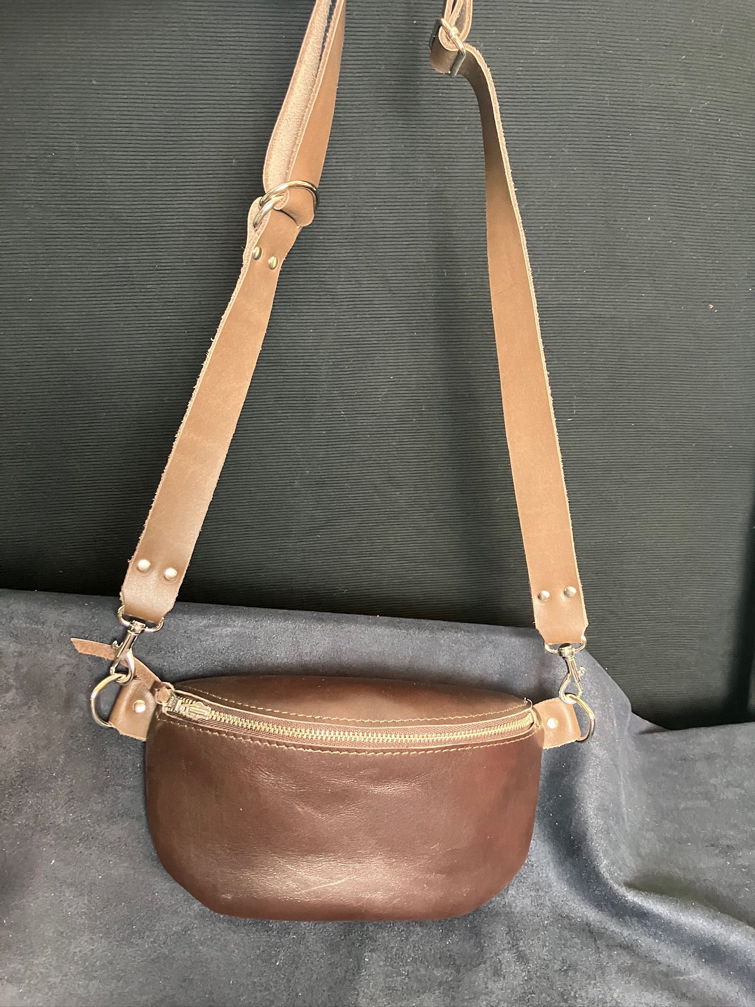 Brown leather crossbody bag with long strap, on a dark blue surface.