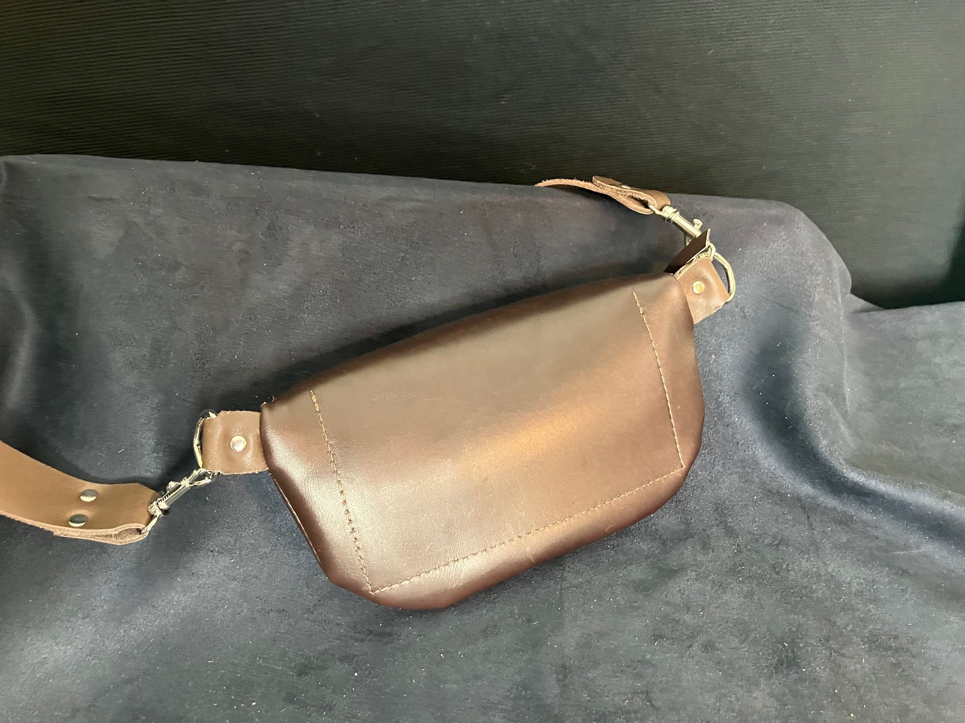 Brown leather fanny pack with strap, resting on dark blue fabric.