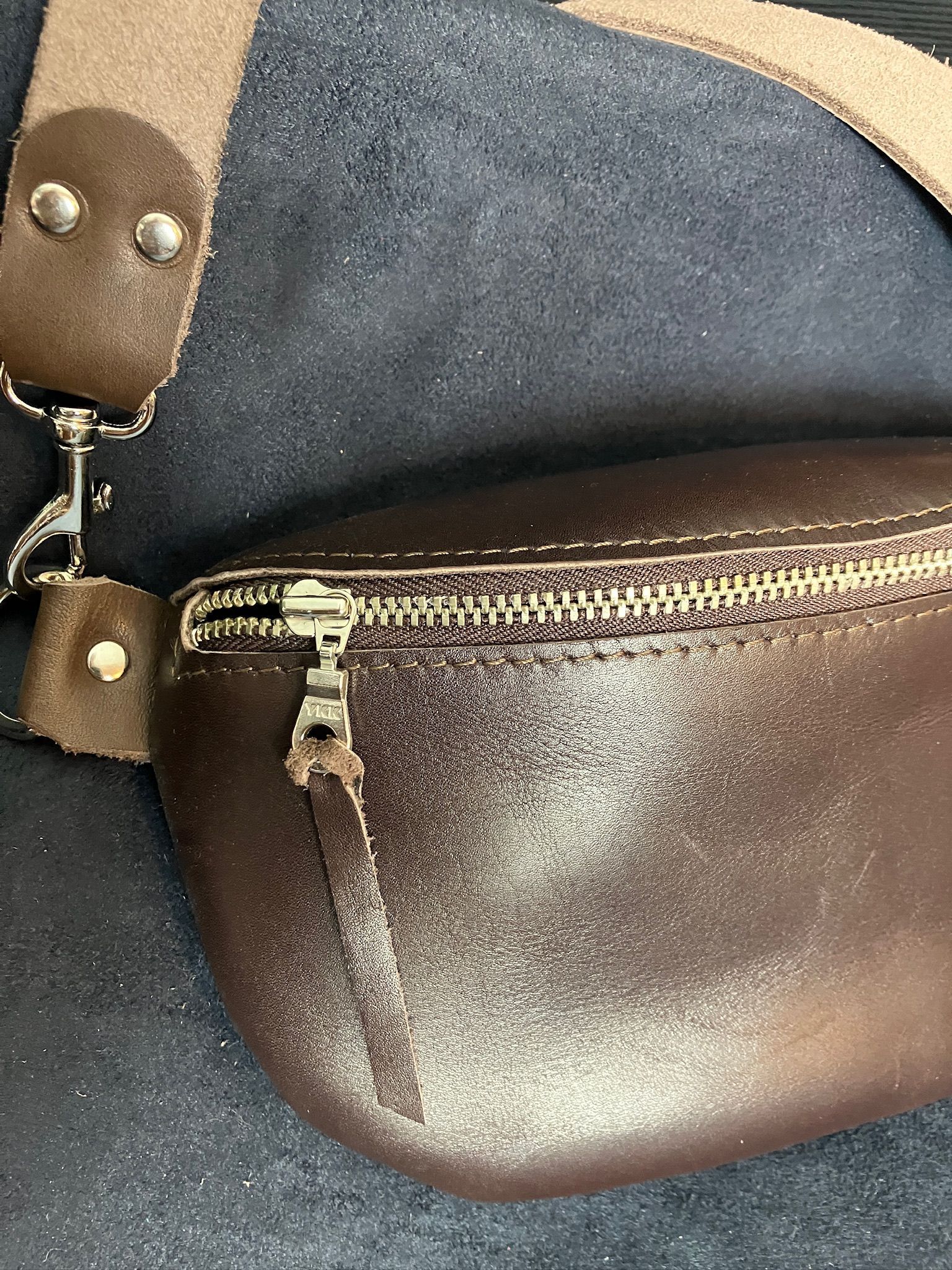 Brown leather fanny pack with silver zipper, metal clasp and strap, on a dark blue surface.