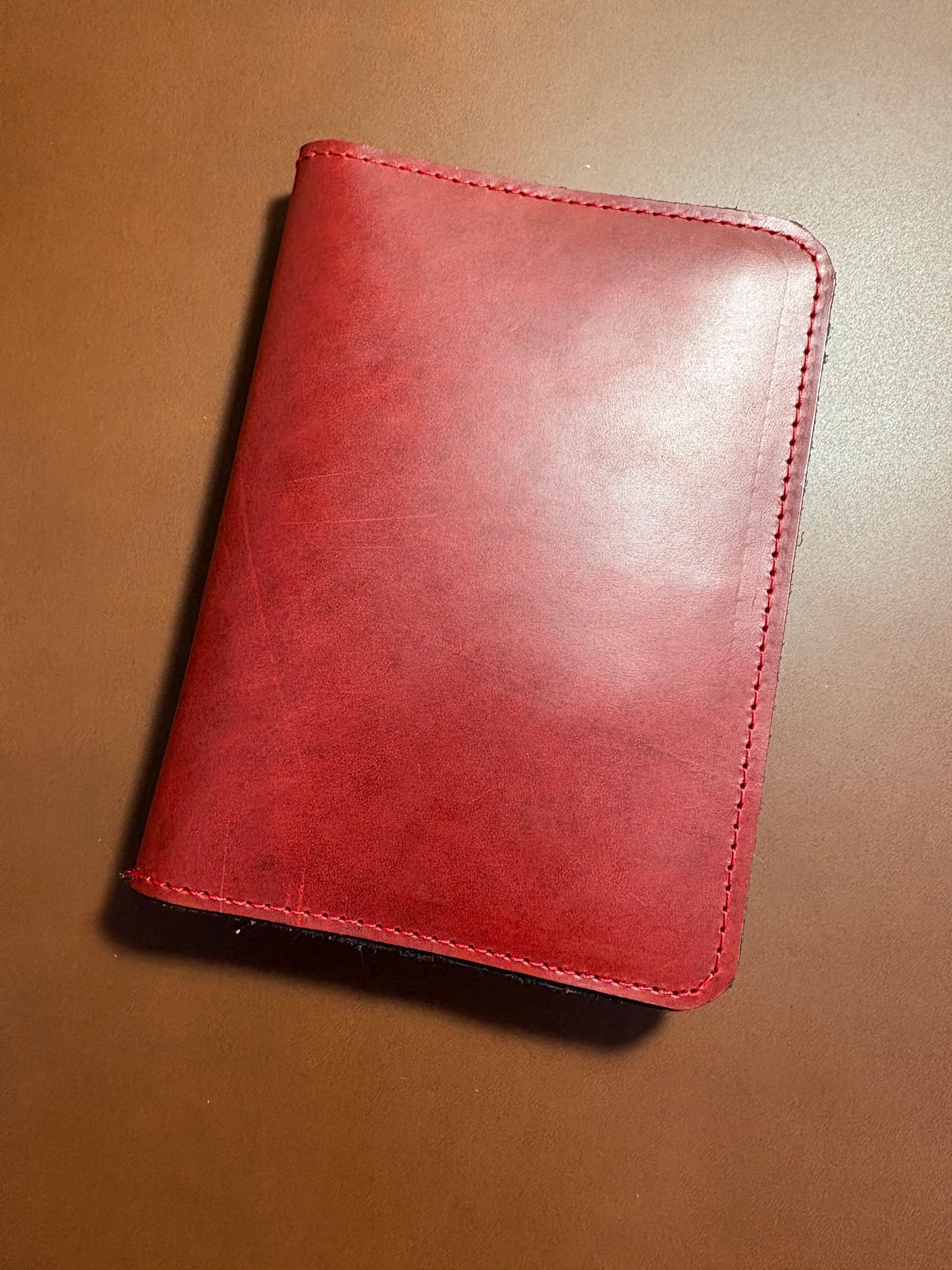 Red leather wallet on a brown surface. Stitched edges are visible.
