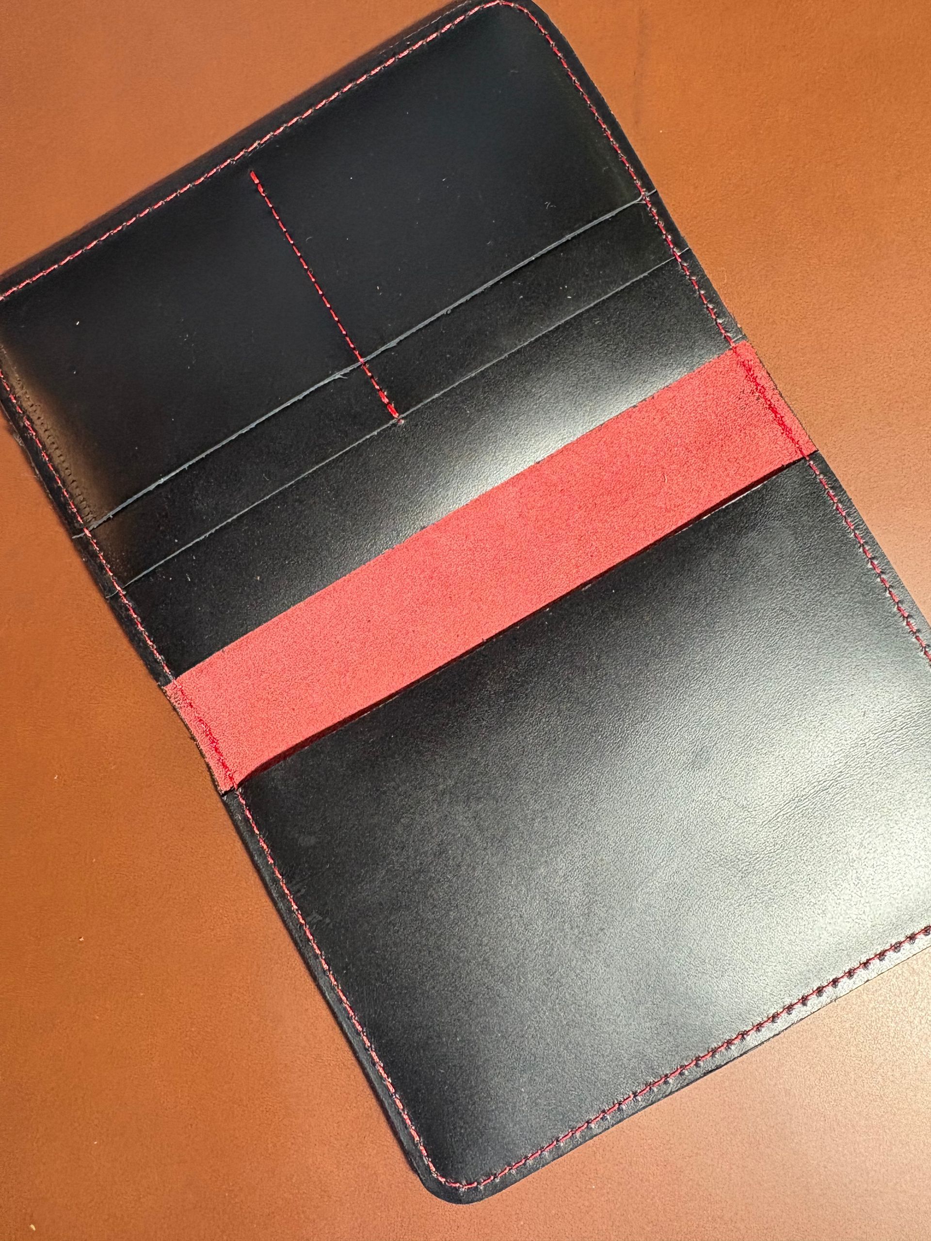 Black leather wallet with red stitching and interior, open on a brown surface.