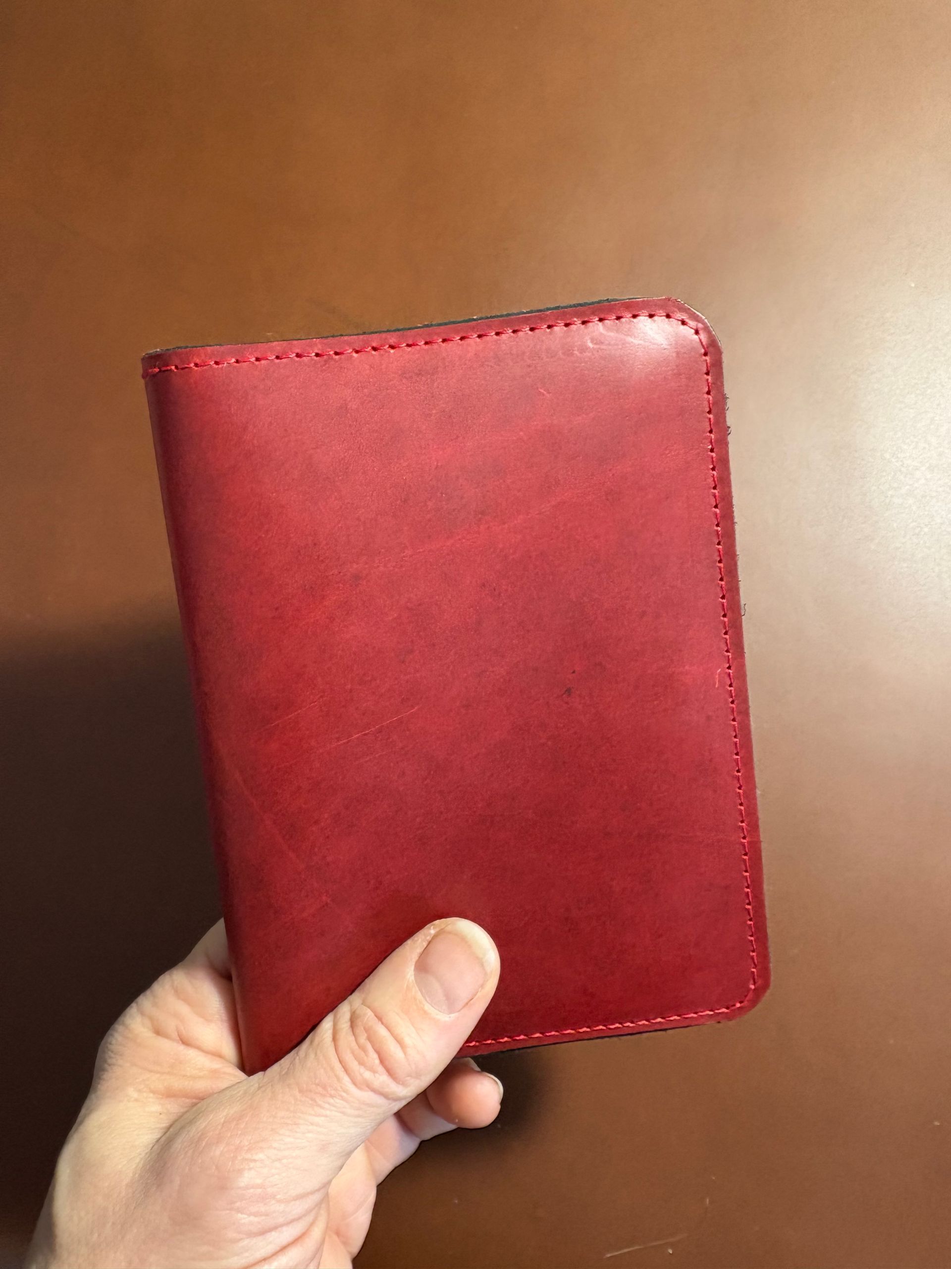 Hand holding a red leather journal on a brown surface.