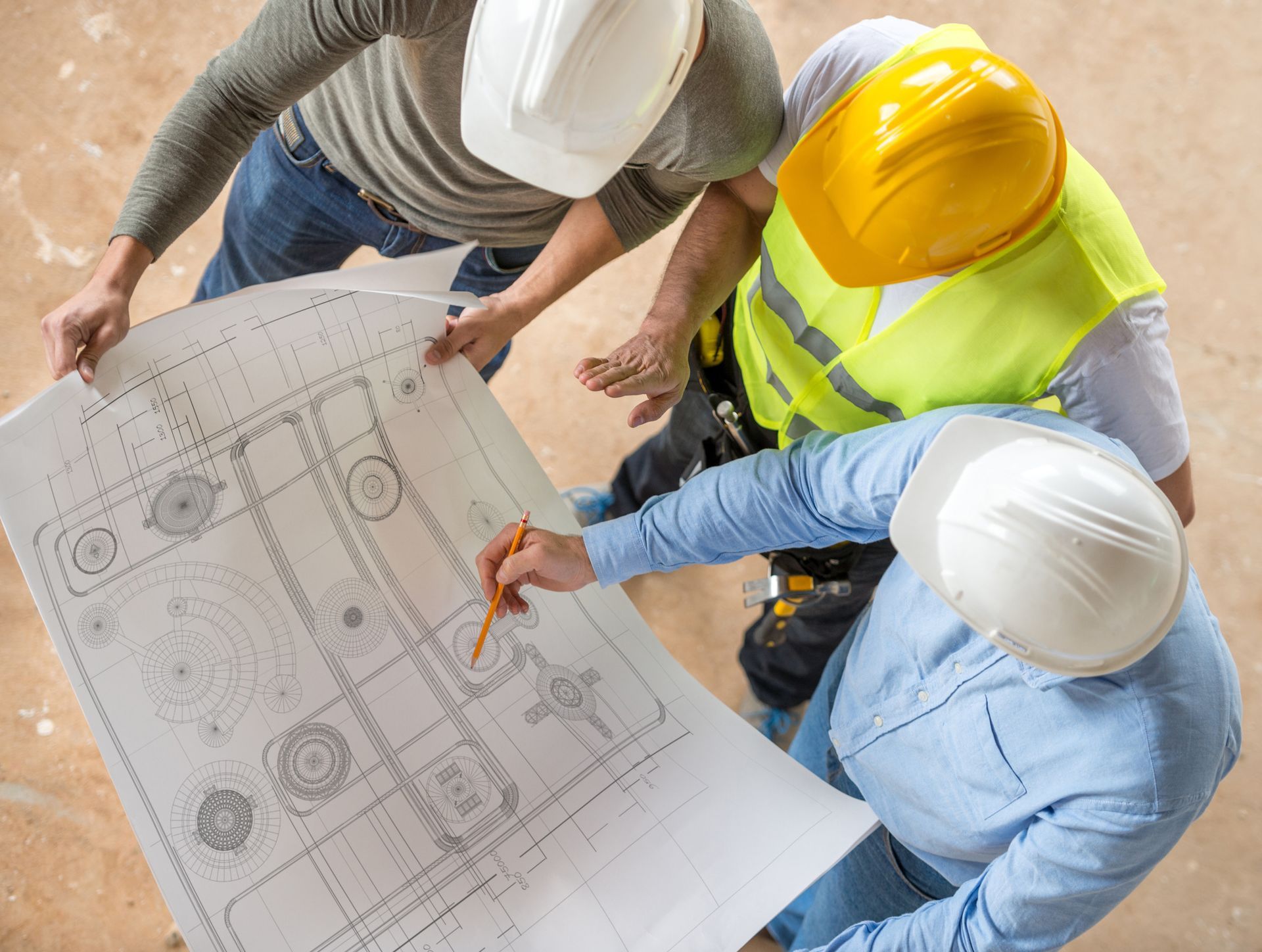 Group of 3 civil engineers wearing helmets as they look at blueprints, on a construction site.