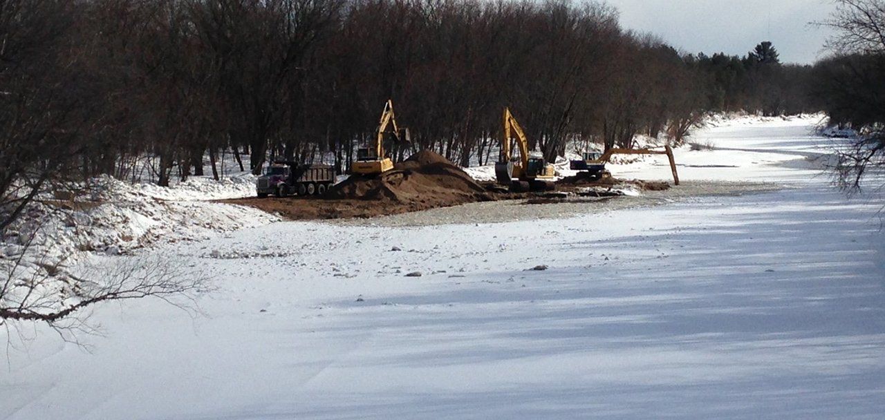 A couple of tractors are working on a snowy river.