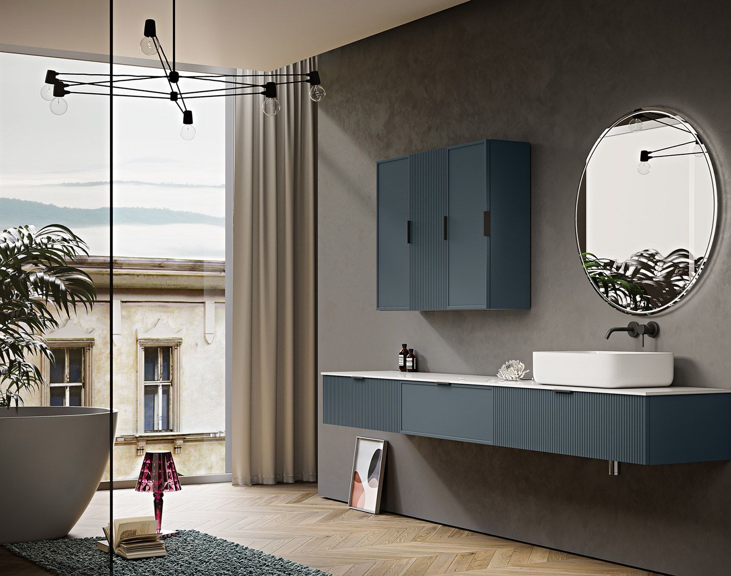Bagno moderno con mobile lavabo e mobiletto blu scanalati, specchio rotondo retroilluminato e vasca freestanding accanto a una finestra.