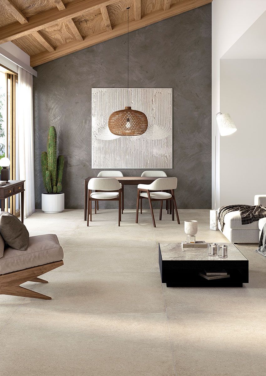 Un moderno soggiorno-sala da pranzo a pianta aperta con soffitti a volta in legno, una parete grigia con finitura materica e mobili dai colori neutri.