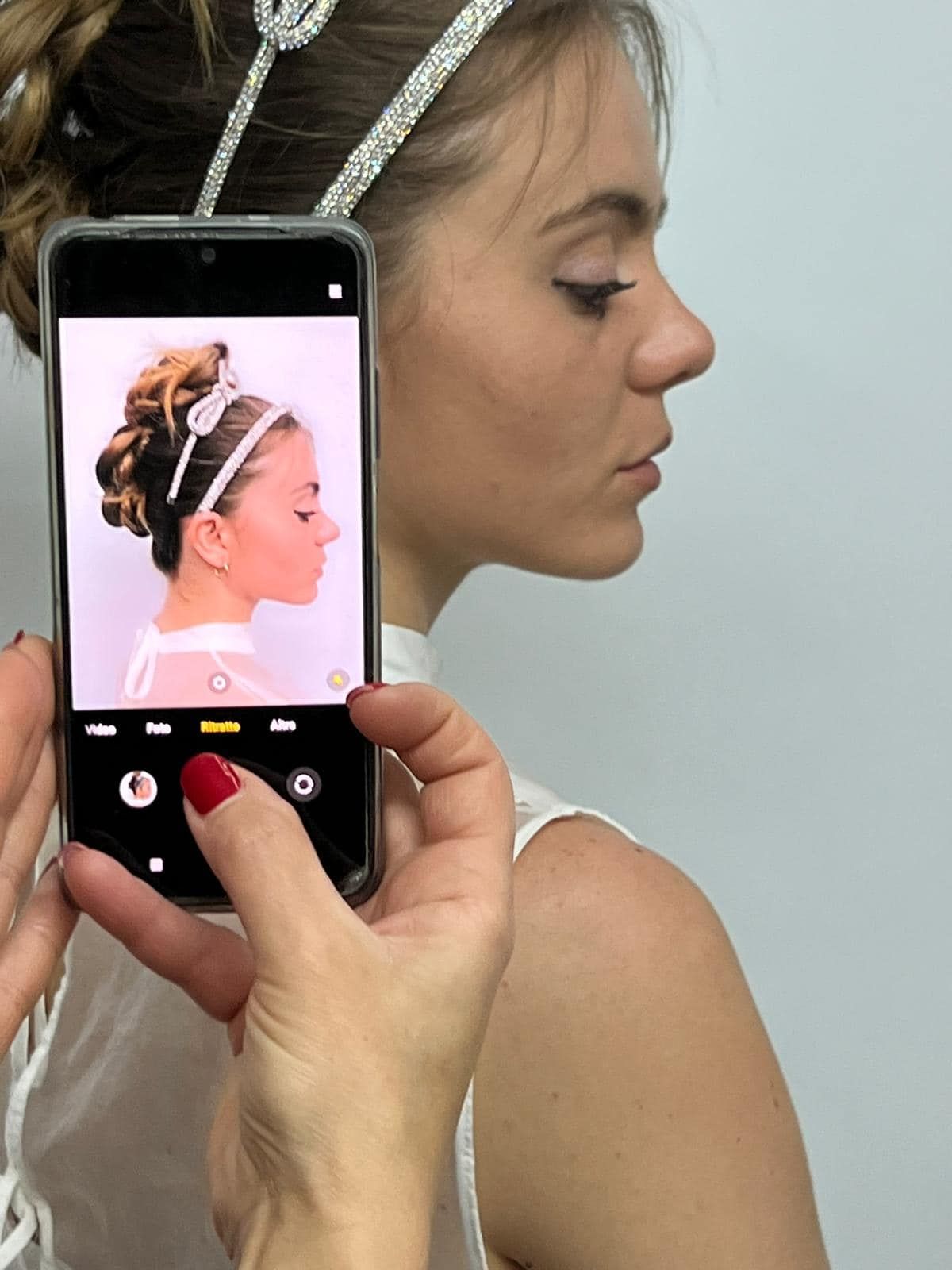 Persona con acconciatura fotografata con il telefono: top bianco, cerchietto argentato, acconciatura raccolta.