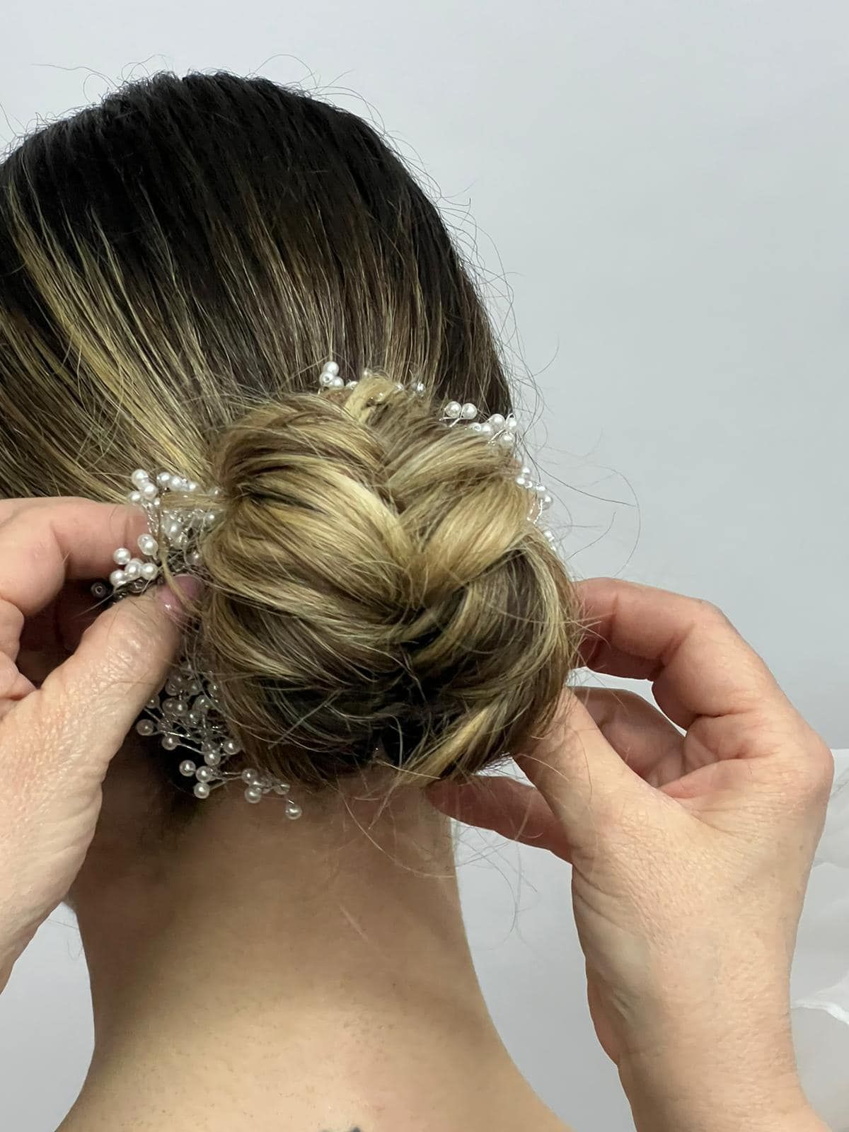 Persona con chignon intrecciato. Mani che sistemano un accessorio per capelli con perle.