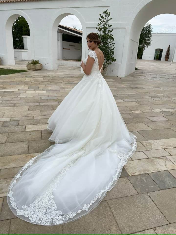 Una donna in abito da sposa bianco con lungo strascico posa all'aperto.