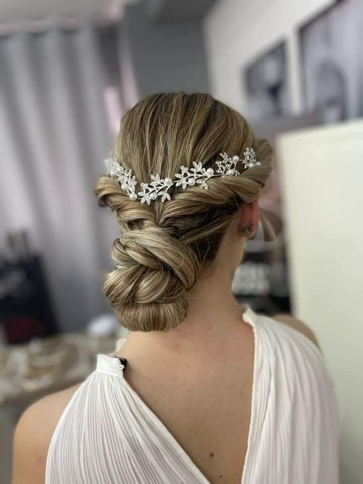 Donna con acconciatura raccolta, adornata con un copricapo floreale, che indossa un abito bianco.